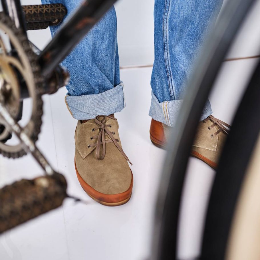 Beige Schuhe an Jeans, neben einem Fahrrad sichtbar.
