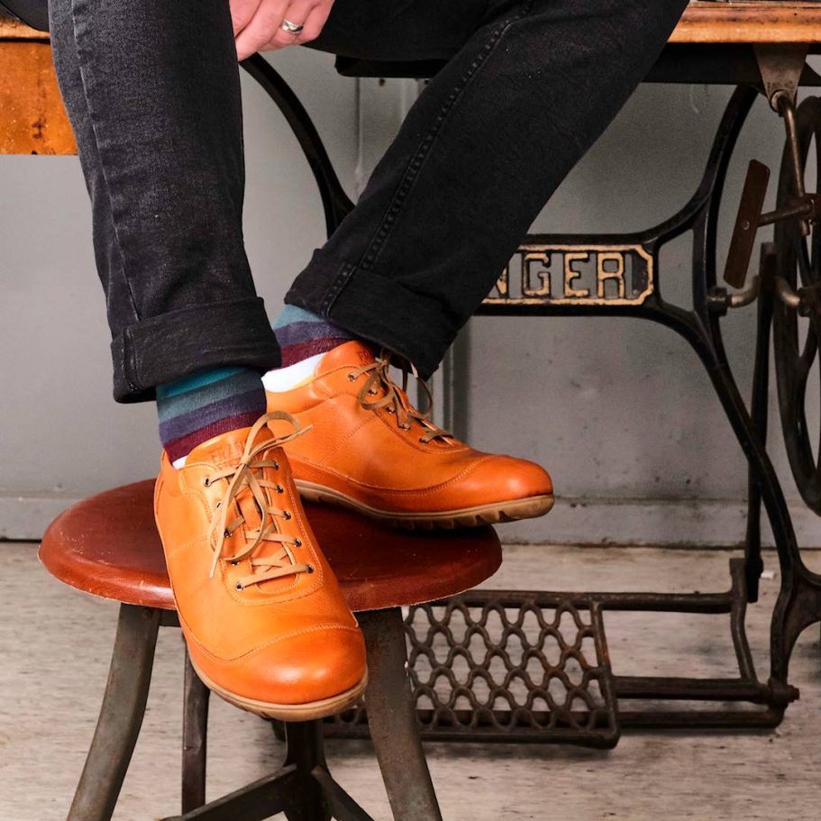 Braune Schuhe auf einem Hocker, getragen von jemandem in dunkler Kleidung.