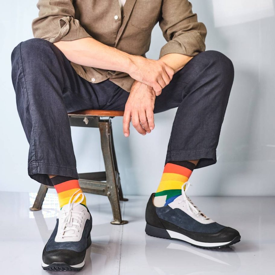 Eine Person sitzt auf einem Hocker, trägt bunte Socken und Schuhe mit sportlichem Stil.